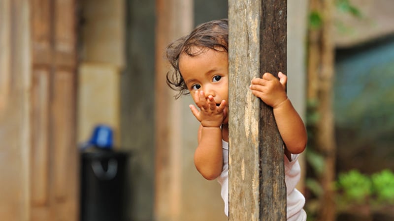 Child hiding behind a wooden post outside. 